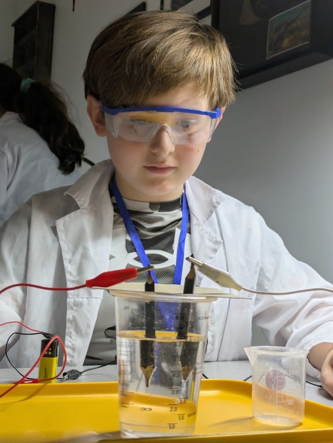Student observing an electrochemistry experiment in a lab coat and goggles