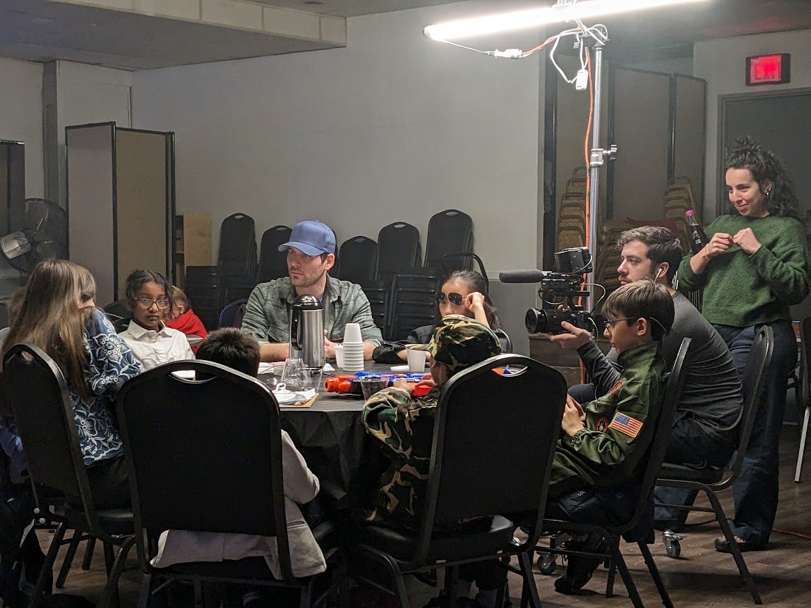 Students around a table on a movie set with camera, microphone and production lighting